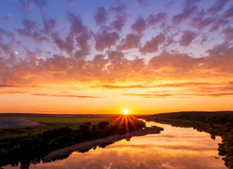 Amazing view at scenic landscape on a beautiful river and colorful sunset with reflection on water surface and glow on a background, spring season landscape