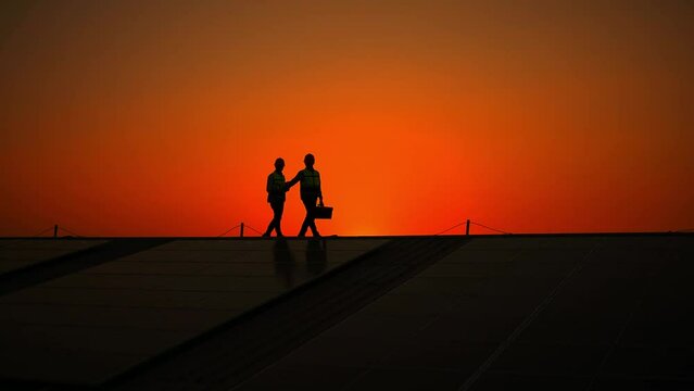 Silhouette engineers walking on roof inspect and check solar cell panel by hold equipment box and radio communication ,solar cell is smart grid ecology energy sunlight alternative power concept.