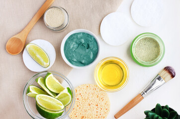 Making homemade skin care treatment facial mask with green clay, lemon citrus essential oil. White table top view view ingredients in jar for home spa beauty treatment, natural detox costmetic product