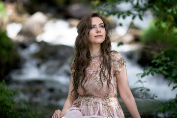 A young woman in a long dress on the background of a mountain waterfall. Enjoyment of nature.