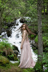 A young woman in a long dress on the background of a mountain waterfall. Enjoyment of nature.
