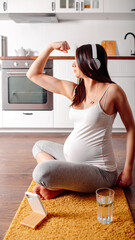 Pregnant doing workout on orange fitness mat. Pragnant yoga at home in the kitchen. Pregnant in white headphones.
