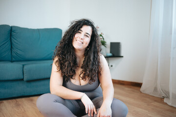 Full length shot of young curvy latina woman in sportswear sitting floor resting while doing fitness yoga at home, latina woman. Happiness new healthy habit. Online class with the laptop concept. - obrazy, fototapety, plakaty