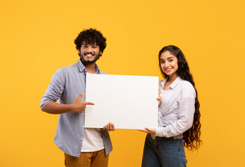 Place for your ad. Portrait of indian couple holding empty blank placard board, pointing at it over...