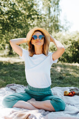 Happy freckled caucasian young woman in straw hat and glasses resting on picnic outdoors. Pretty...