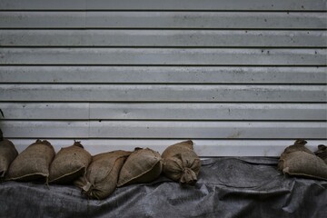 Dirty white house wall with row of sandbags on black tarp.  Room for copy.