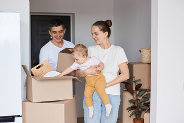 Portrait of positive happy family, mother, father and daughter posing in a new house after moving...