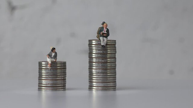 Miniature men and miniature women sitting on coins of different heights. Concept of gender pay gap.

