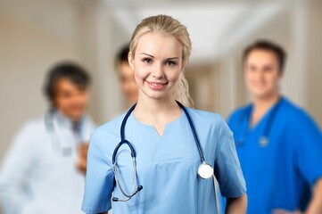 Portrait of happy young nurse in uniform with healthcare team in background. Successful doctor and nurses