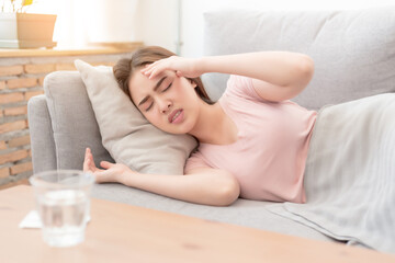 Portrait of Asian woman is holding their hand from headache lying on sofa, Young beautiful Asian woman on sofa having headache / migraine / stress / sick