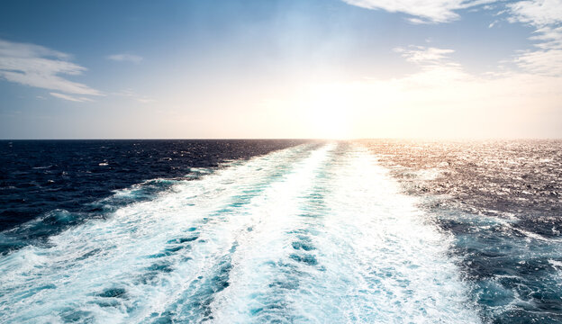 Foamy trail in the sea of ​​a sailing cruise ship sailing away at sunset.