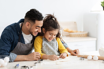 Cute little arab girl cutting different cookie shapes from dough with dad