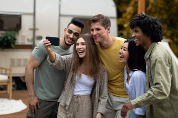Happy multiracial friends taking selfie near their trailer, smiling and having fun together during autumn camping trip