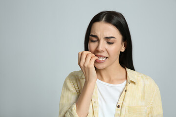 Young woman biting her nails on light grey background. Space for text - obrazy, fototapety, plakaty