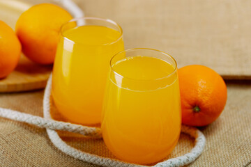 Two glasses of juice with oranges around.