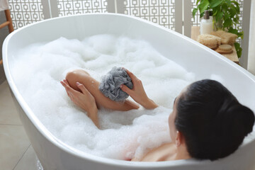 Woman taking bath with mesh pouf in bathroom