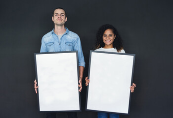 Portait of happy mixed race couple holding blank photo frame and looking at camera against blackgray background. Mock-up banner, Empty space for the text.