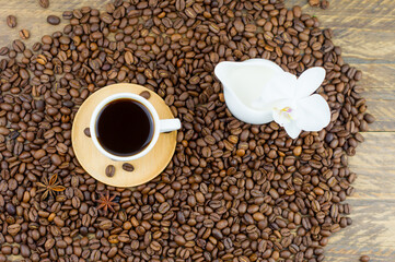 top view of a small cup of black coffee and a jug milk standing on coffee beans. wooden background, white orchid flower.