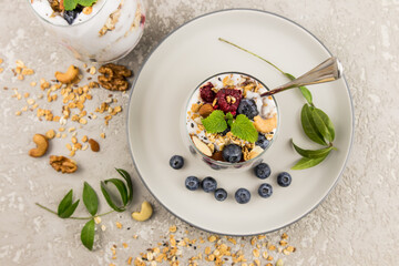 natural yogurt with granola and berries in a glass beaker on a ceramic plate and concrete background. light breakfast, healthy food.