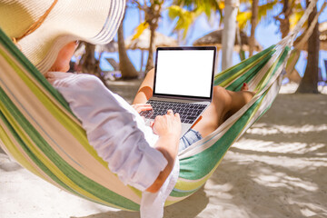 Woman relaxing in hammock on tropical beach and using laptop computer