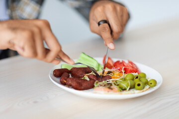 Unrecognizable guy cutting fresh vegetables and sausages, closeup photo
