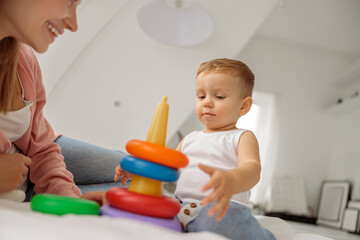 Cute little boy playing with a colorful toy near his mom