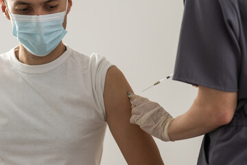 COVID-19 vaccine injection, doctor in gloves holds syringe and makes jab to woman patient in...