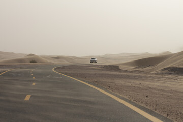 Fototapeta na wymiar Dusty desert road in sand storm with car