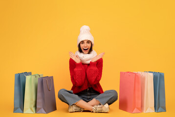 Shopaholic concept. Happy lady in knitted hat and sweater sitting among colorful shopping bags on...