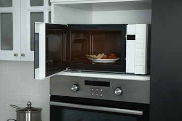 Open microwave oven with food on white shelf in kitchen