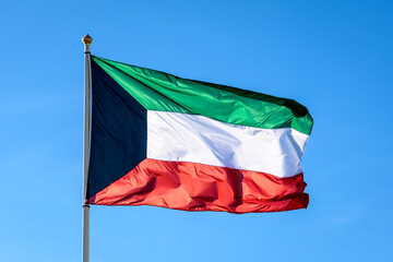 The national flag of Kuwait is flying in the wind at full mast against blue sky.