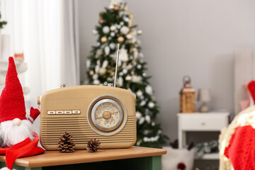 Stylish radio and Christmas gnome on wooden table in decorated room. Space for text