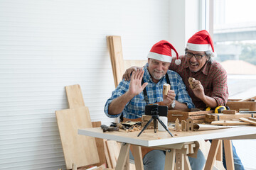 Happy two senior carpenter men Caucasian and asian with beard wearing santa hat selling and showing...