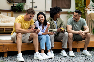 Diverse friends sitting near camper van, speaking to each other, spending great time together on camping trip in autumn