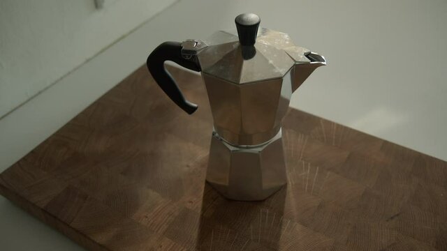 Young hipster placing Bialetti Moka Express Coffee on a wooden cutting board in the morning in the kitchen at home