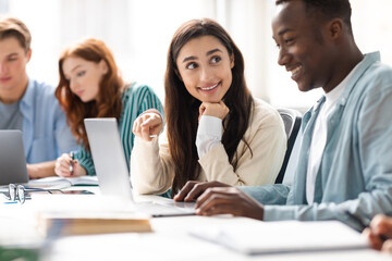 Smiling diverse students sitting at desk working on group project