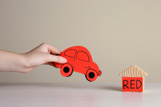 Woman holding red car near wooden house at white table, closeup. ABA therapy concept