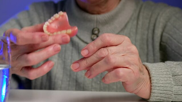 Elderly woman takes false teeth or denture and puts it on.