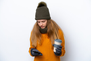 Teenager Russian girl wearing winter jacket isolated on white background holding coffee to take away and a mobile