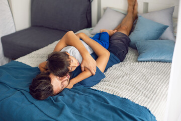 bearded father hugs his baby boy lying on bed in a white bedroom