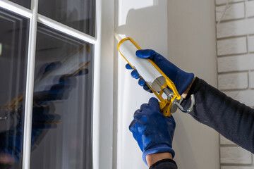 Worker is applying polyurethane foam to fill gap between sash and window frame. Creating comfort...