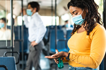 Black woman going by bus, using sanitizer on hands - obrazy, fototapety, plakaty