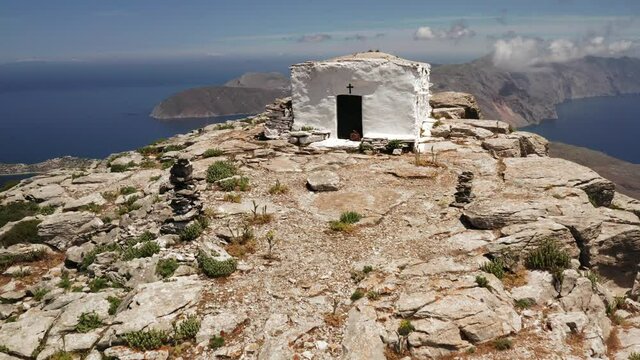 Drone shot of cute little chapel in Greece on a rocky peak, Amorgos Island in cyclades Aegean Sea with beautiful panorama of blue ocean and mountains