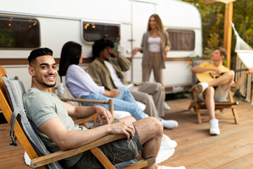 Group of multiracial young friends having outdoor party near camper van, playing guitar, having fun...