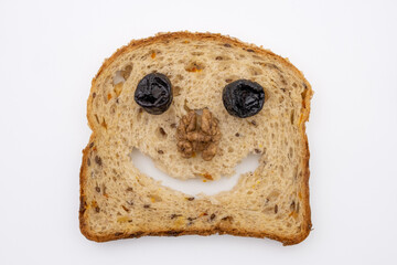 Funny face made from a slice of multigrain bread, dried plums and walnut. Joyful healthy food. Top view on white background.