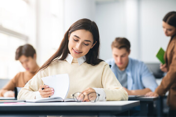 Smiling student sitting at desk in classroom writing in notebook