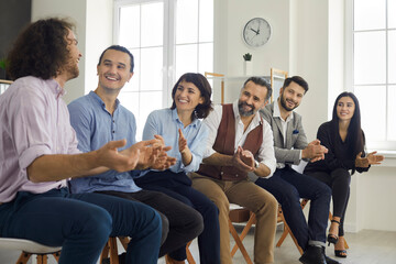 A group of young office colleagues at a seminar, smiling and applauding their male colleague for an...