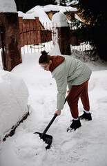 Adorable teen age girl in warm jacket helping family to clean yard from snow with snow shovel