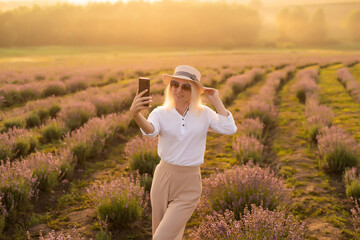 Beautiful young healthy woman with a white dress running joyfully through a lavender field holding a straw hat under the rays of the setting sun