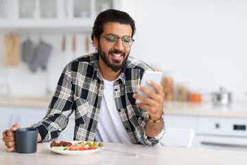 Smiling middle-eastern man eating healthy food and using phone